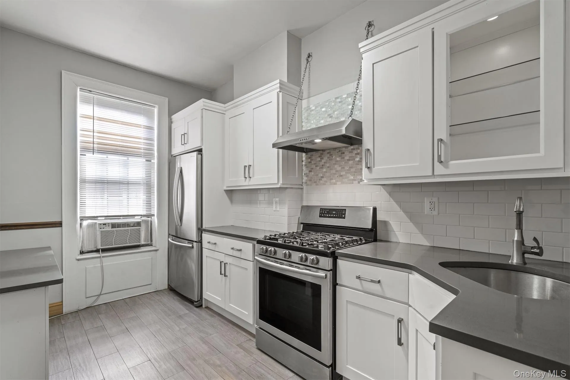 Kitchen with stainless steel appliances, white cabinetry, light wood-style flooring, and dark stone counters Kitchen with stainless steel appliances, white cabinetry, light wood-style flooring, and dark stone counters