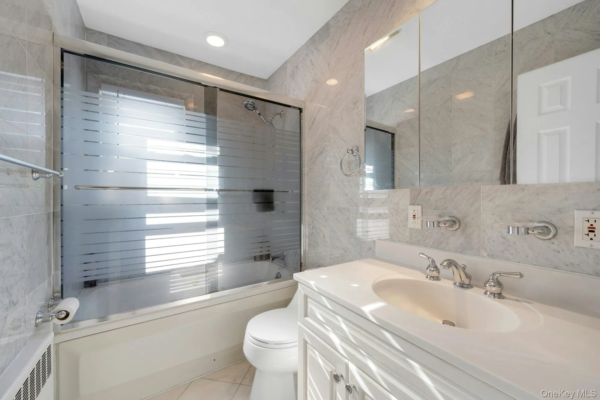 Full bathroom with vanity, radiator, combined bath / shower with glass door, toilet, and tile walls Full bathroom with vanity, radiator, combined bath / shower with glass door, toilet, and tile walls