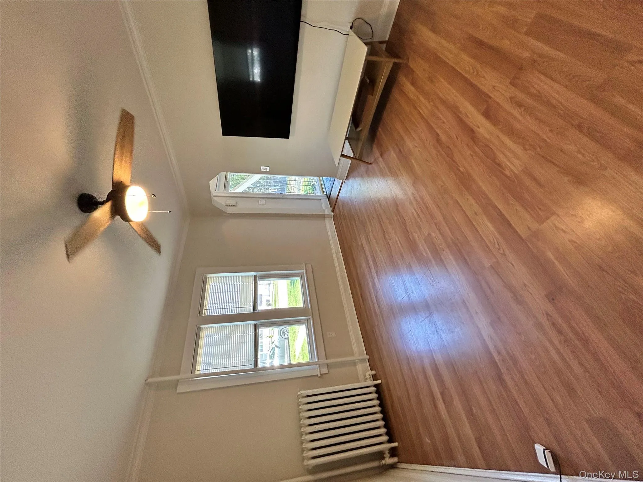 Unfurnished living room with ceiling fan, radiator heating unit, baseboards, wood finished floors, and ornamental molding Unfurnished living room with ceiling fan, radiator heating unit, baseboards, wood finished floors, and ornamental molding