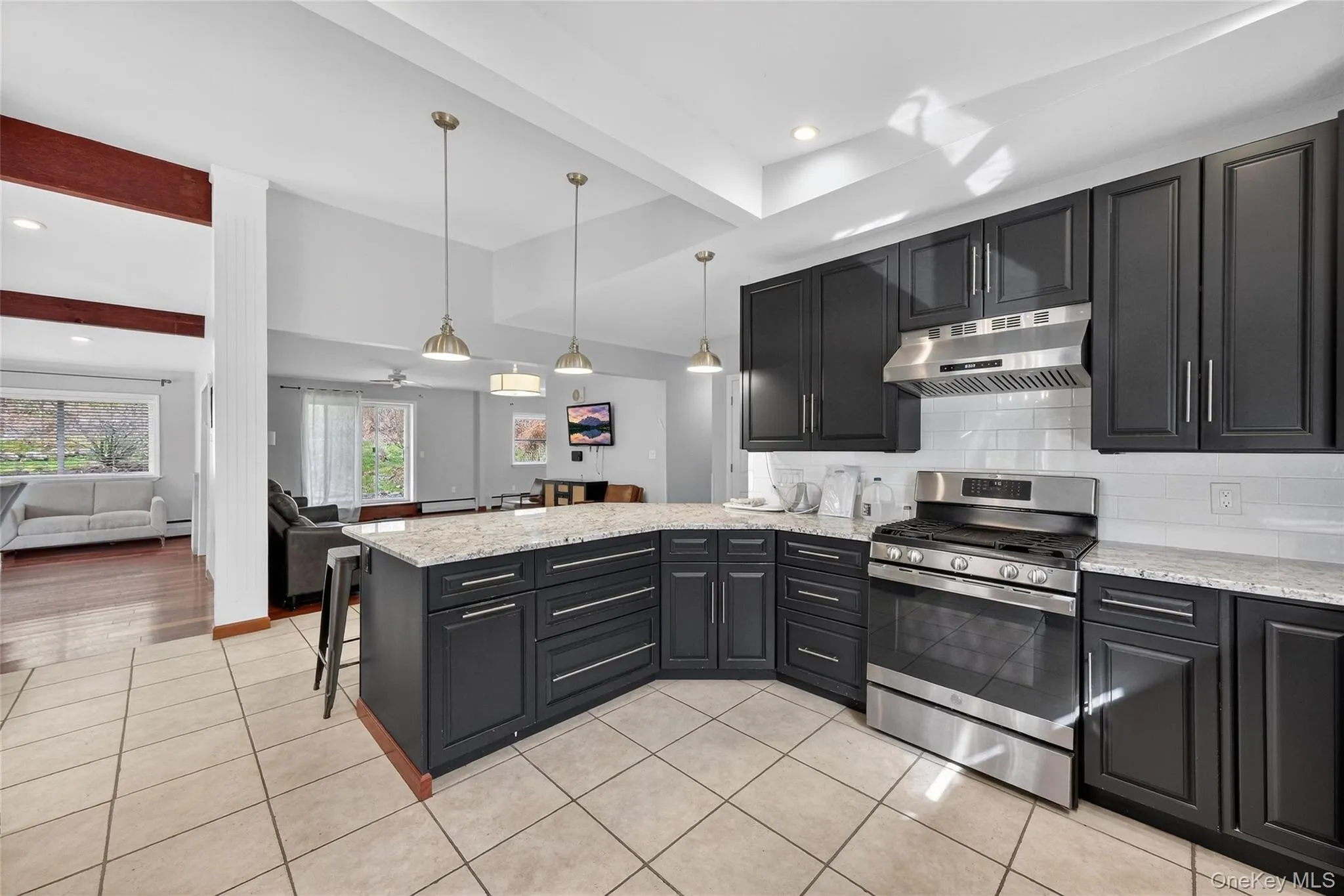 Kitchen featuring dark cabinets, beam ceiling, stainless steel gas range, decorative backsplash, and light stone counters Kitchen featuring dark cabinets, beam ceiling, stainless steel gas range, decorative backsplash, and light stone counters