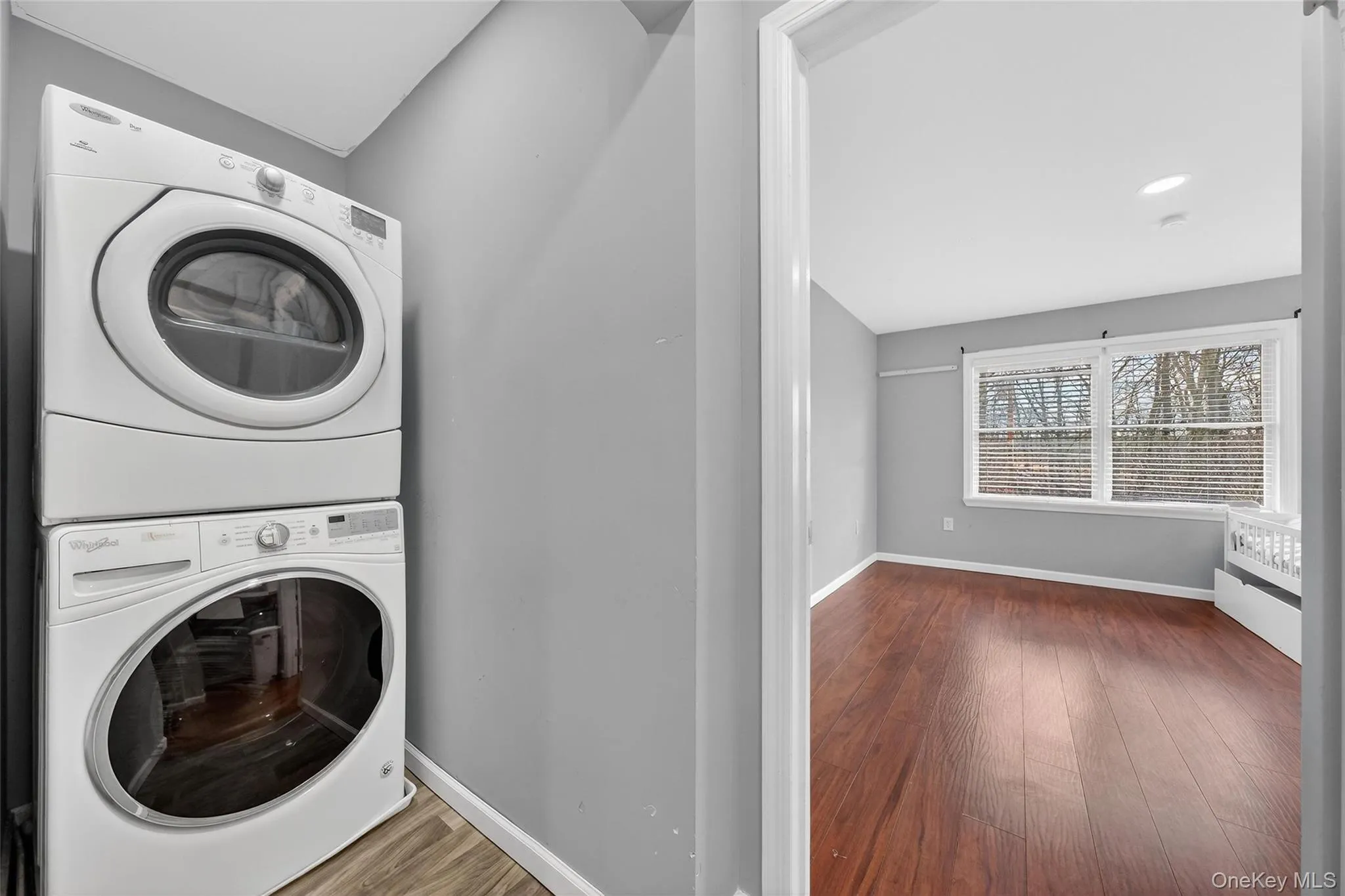 Laundry room with dark wood-style flooring and stacked washer / dryer Laundry room with dark wood-style flooring and stacked washer / dryer