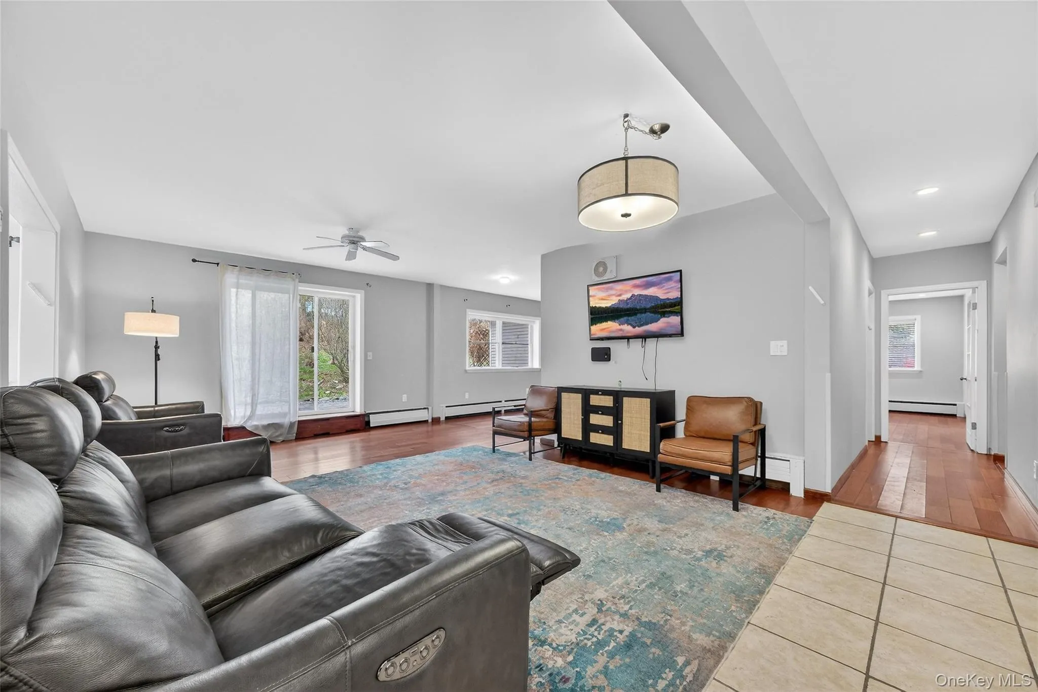 Living room featuring healthy amount of natural light, ceiling fan, tile patterned flooring, and a baseboard heating unit Living room featuring healthy amount of natural light, ceiling fan, tile patterned flooring, and a baseboard heating unit