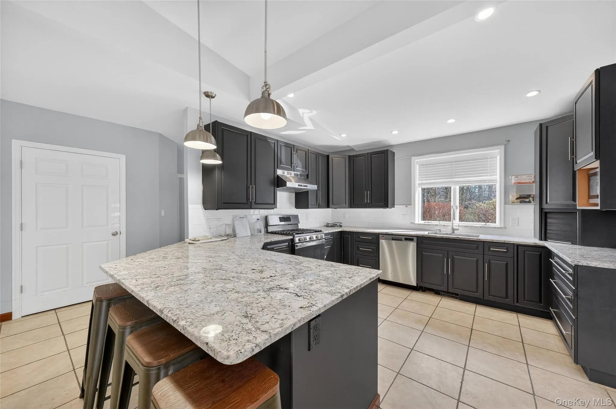 Kitchen featuring a kitchen breakfast bar, backsplash, a peninsula, stainless steel appliances, and light stone counters Kitchen featuring a kitchen breakfast bar, backsplash, a peninsula, stainless steel appliances, and light stone counters