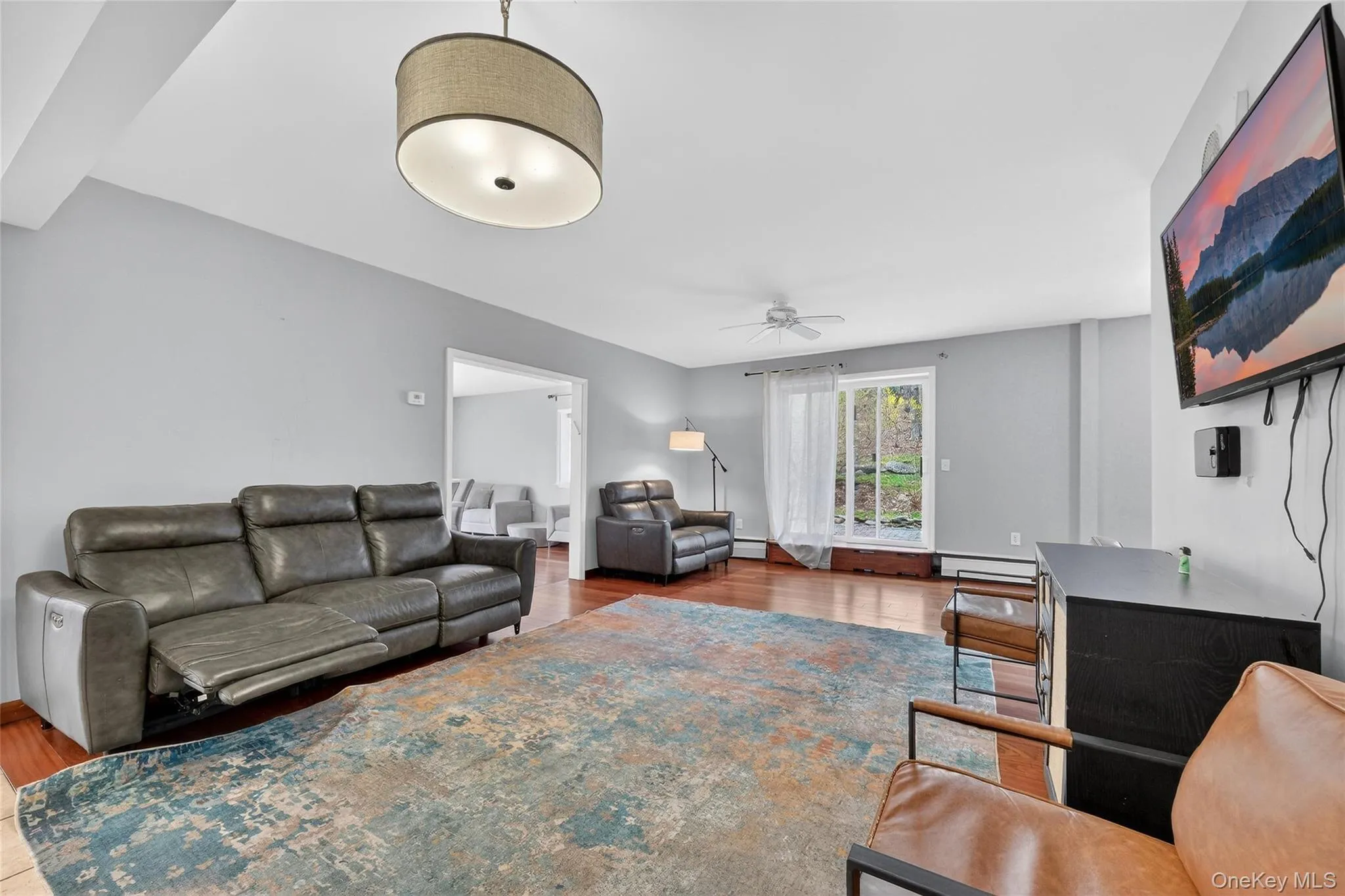 Living room featuring light wood-type flooring, a ceiling fan, and baseboard heating Living room featuring light wood-type flooring, a ceiling fan, and baseboard heating