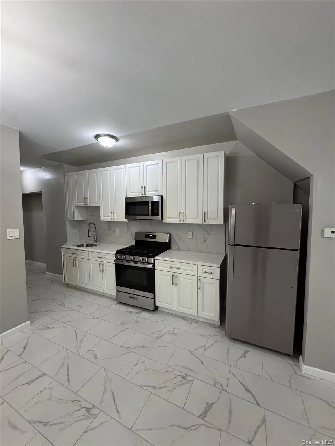 Kitchen featuring decorative backsplash, stainless steel appliances, light marble finish flooring, white cabinets, and light stone counters Kitchen featuring decorative backsplash, stainless steel appliances, light marble finish flooring, white cabinets, and light stone counters