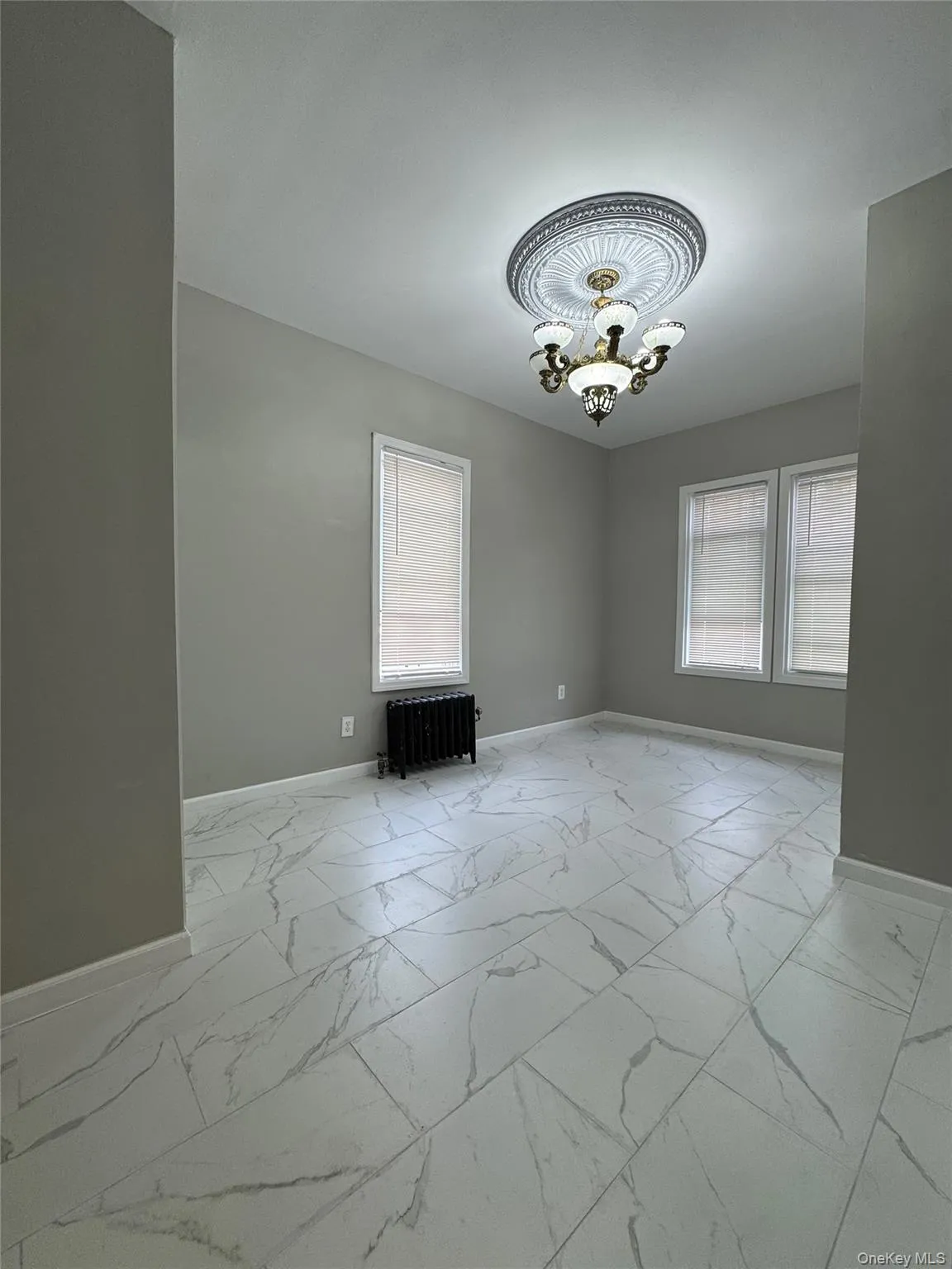 Unfurnished room with light marble finish flooring, healthy amount of natural light, radiator heating unit, and a chandelier Unfurnished room with light marble finish flooring, healthy amount of natural light, radiator heating unit, and a chandelier