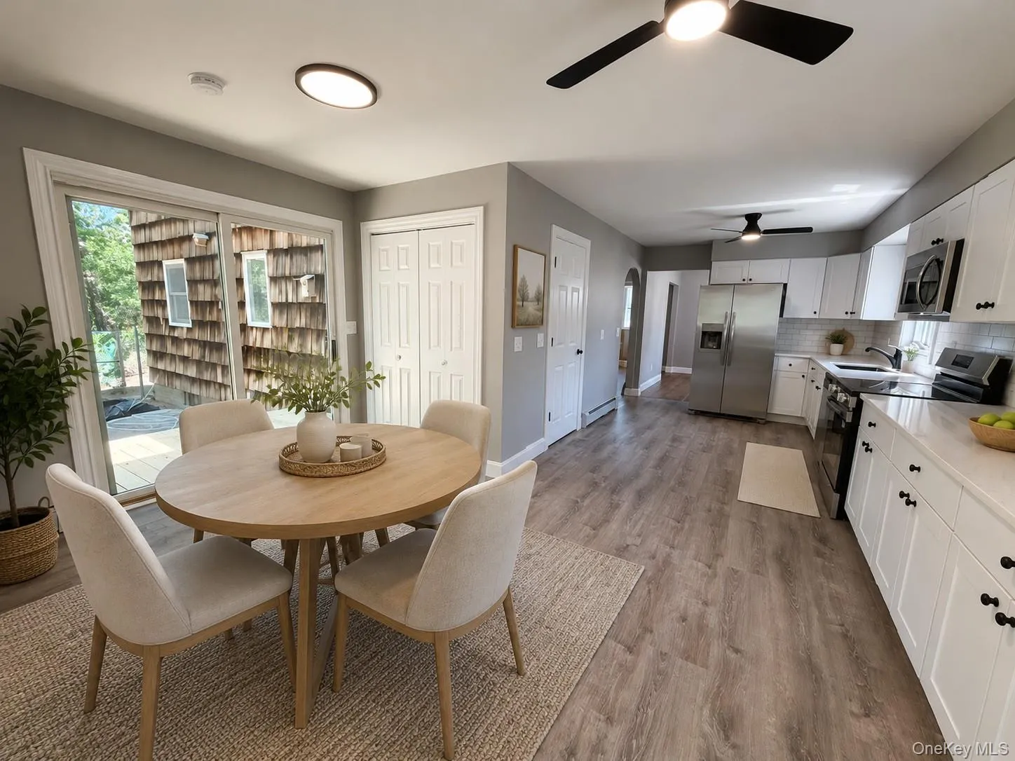 AI Staged- Open-concept kitchen and dining area featuring wood-finish flooring, white cabinetry with black hardware, and stainless steel appliances AI Staged- Open-concept kitchen and dining area featuring wood-finish flooring, white cabinetry with black hardware, and stainless steel appliances