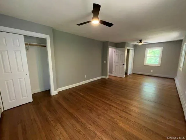 Spacious room featuring rich wood-finish flooring, light gray walls, two ceiling fans with integrated lighting, and multiple windows Spacious room featuring rich wood-finish flooring, light gray walls, two ceiling fans with integrated lighting, and multiple windows