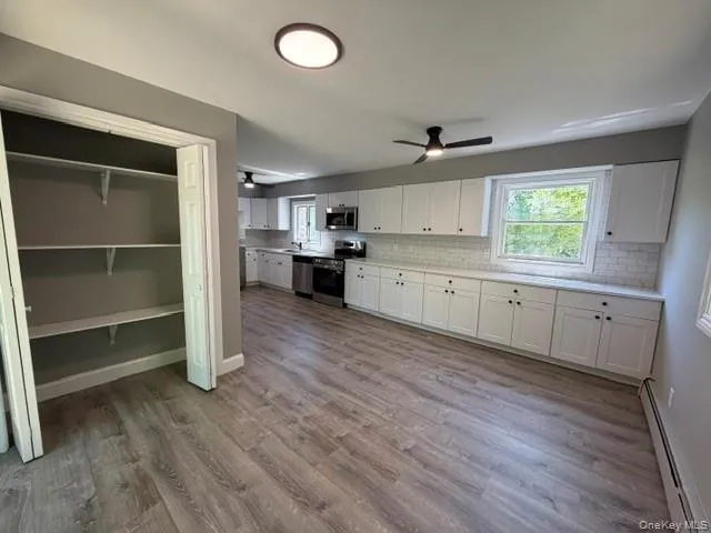 Spacious kitchen featuring extensive white cabinetry, subway tile backsplash, stainless steel appliances, a ceiling fan, and wood-finish flooring Spacious kitchen featuring extensive white cabinetry, subway tile backsplash, stainless steel appliances, a ceiling fan, and wood-finish flooring