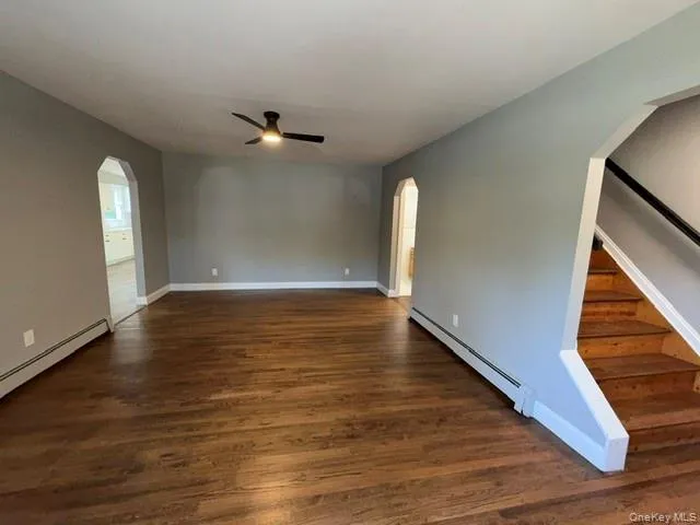 Spacious living area featuring wood-finish flooring, a contemporary ceiling fan with integrated lighting, and neutral wall tones Spacious living area featuring wood-finish flooring, a contemporary ceiling fan with integrated lighting, and neutral wall tones
