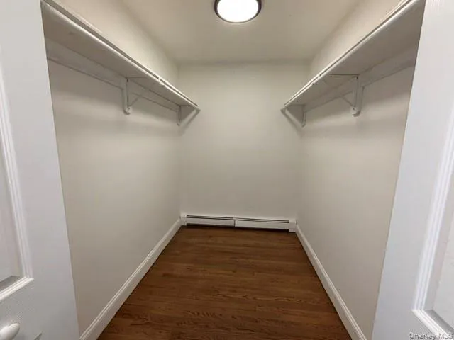 Walk-in closet featuring wood-finish flooring, white walls, and built-in shelving with hanging rods Walk-in closet featuring wood-finish flooring, white walls, and built-in shelving with hanging rods