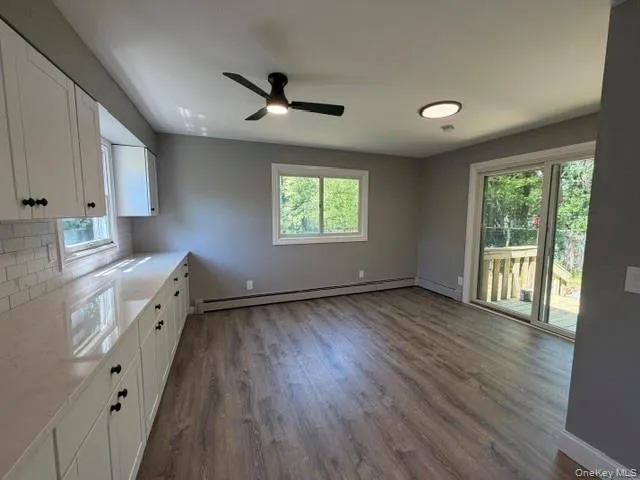Open-concept living space with wood-finish flooring, white cabinetry, light-toned countertops, and a subway tile backsplash Open-concept living space with wood-finish flooring, white cabinetry, light-toned countertops, and a subway tile backsplash