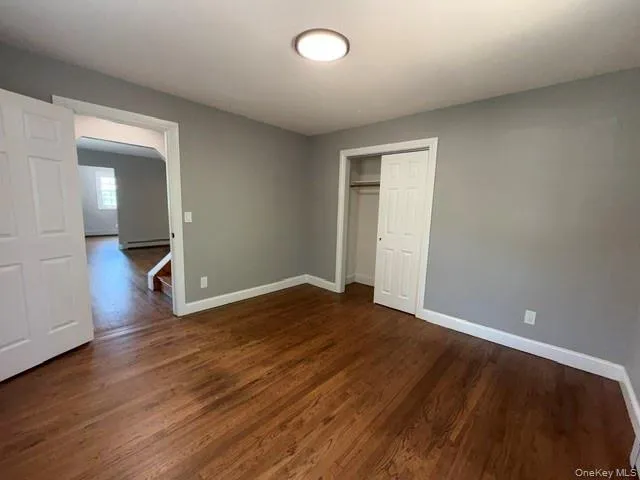 Interior room featuring wood-finish flooring, light gray walls, a ceiling-mounted light fixture, white baseboards, and a built-in closet with bi-fold doors Interior room featuring wood-finish flooring, light gray walls, a ceiling-mounted light fixture, white baseboards, and a built-in closet with bi-fold doors