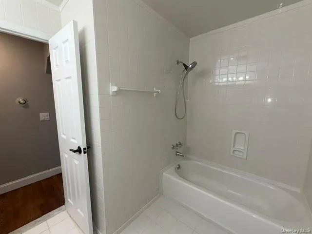 Bathroom featuring a white tiled shower and tub combination with a built-in soap dish Bathroom featuring a white tiled shower and tub combination with a built-in soap dish
