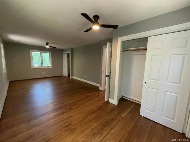 Spacious room featuring wood-finish flooring, light grey walls, two ceiling fans with integrated lighting, and a white sliding closet door Spacious room featuring wood-finish flooring, light grey walls, two ceiling fans with integrated lighting, and a white sliding closet door