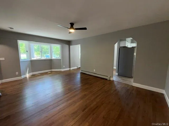 Spacious living area featuring rich wood-finish flooring, a contemporary ceiling fan, and a wide bay window Spacious living area featuring rich wood-finish flooring, a contemporary ceiling fan, and a wide bay window