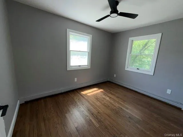 Interior room featuring wood-finish flooring, two white-framed windows, and a black ceiling fan Interior room featuring wood-finish flooring, two white-framed windows, and a black ceiling fan