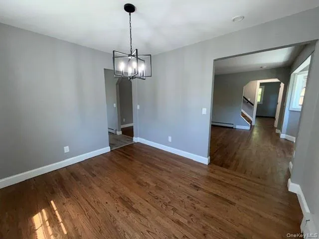 Spacious room featuring wood-finish flooring, light gray wall paint, and white baseboards Spacious room featuring wood-finish flooring, light gray wall paint, and white baseboards