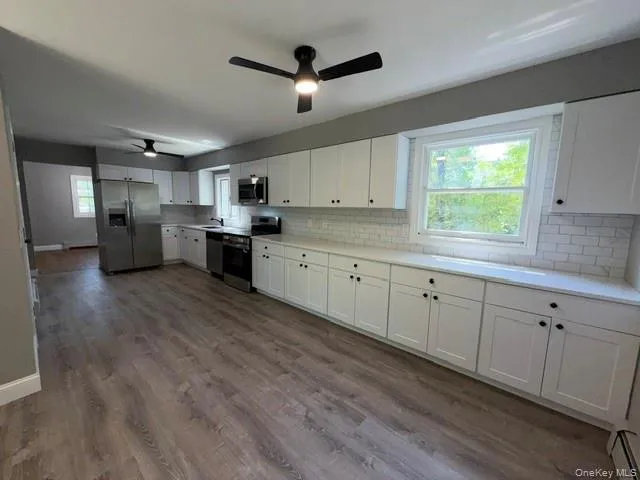 Spacious kitchen featuring extensive white cabinetry, light countertops, wood-finish flooring, and white subway tile backsplash Spacious kitchen featuring extensive white cabinetry, light countertops, wood-finish flooring, and white subway tile backsplash