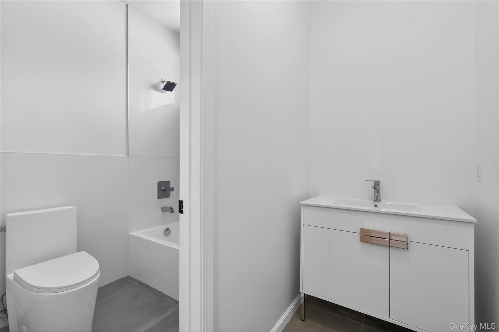 Full bathroom with vanity, tile walls, bathing tub / shower combination, and dark tile patterned floors Full bathroom with vanity, tile walls, bathing tub / shower combination, and dark tile patterned floors