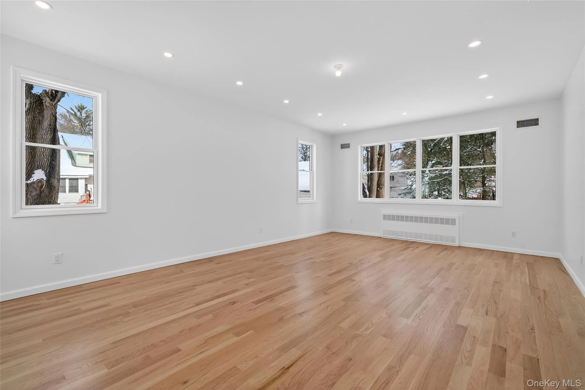 Unfurnished room with light wood finished floors, radiator heating unit, plenty of natural light, and recessed lighting Unfurnished room with light wood finished floors, radiator heating unit, plenty of natural light, and recessed lighting