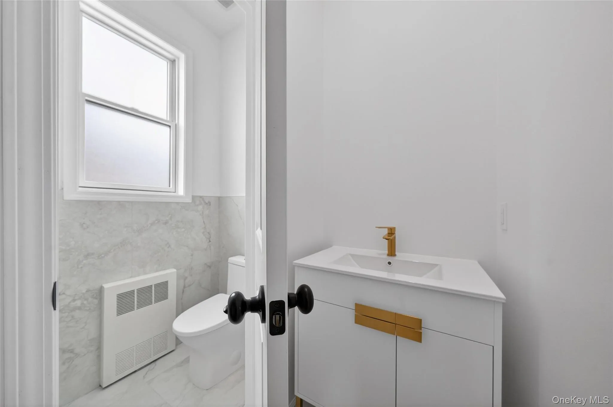 Bathroom with marble look tile flooring, radiator, vanity, tile walls, and a wainscoted wall Bathroom with marble look tile flooring, radiator, vanity, tile walls, and a wainscoted wall