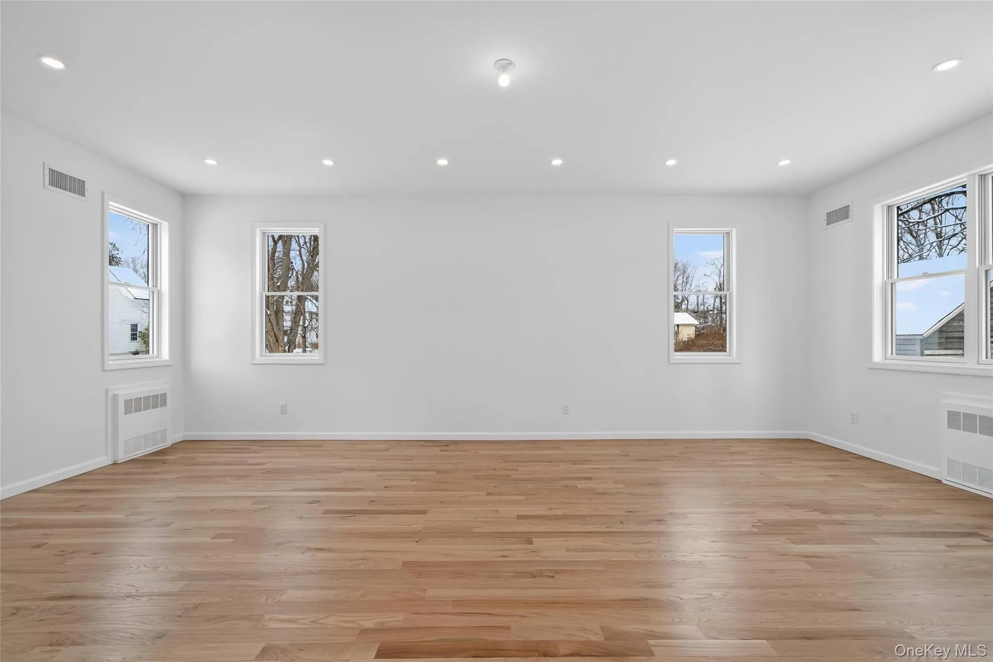 Empty room with recessed lighting, plenty of natural light, light wood-style floors, and radiator Empty room with recessed lighting, plenty of natural light, light wood-style floors, and radiator