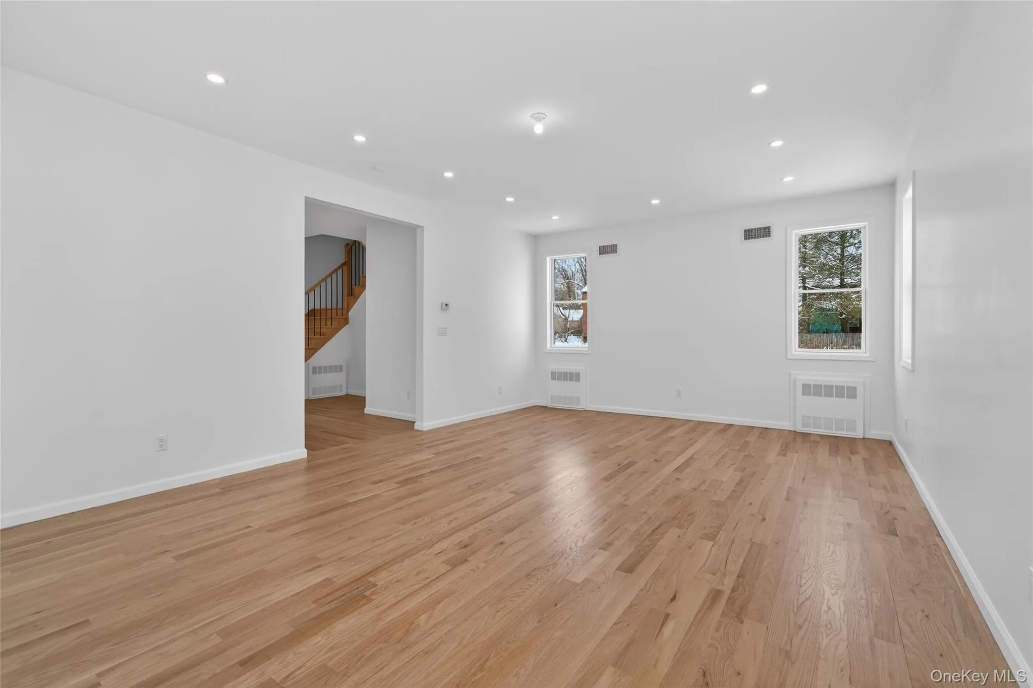 Empty room with recessed lighting, light wood finished floors, plenty of natural light, stairs, and radiator heating unit Empty room with recessed lighting, light wood finished floors, plenty of natural light, stairs, and radiator heating unit