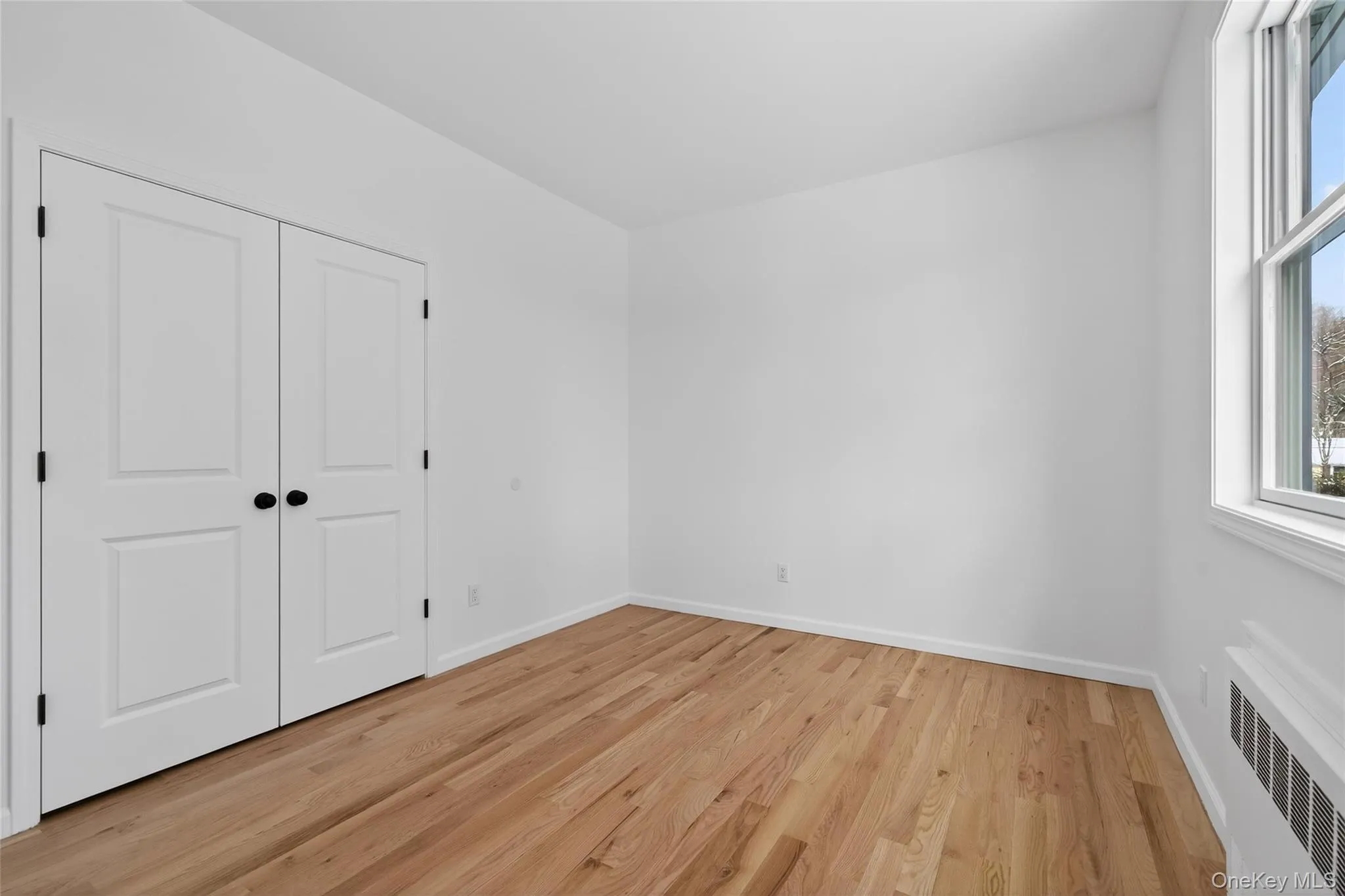 Unfurnished bedroom featuring radiator, light wood-style flooring, and a closet Unfurnished bedroom featuring radiator, light wood-style flooring, and a closet