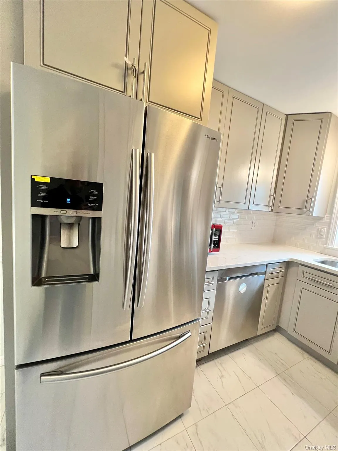 Kitchen with decorative backsplash, gray cabinets, light countertops, marble finish floor, and stainless steel appliances Kitchen with decorative backsplash, gray cabinets, light countertops, marble finish floor, and stainless steel appliances