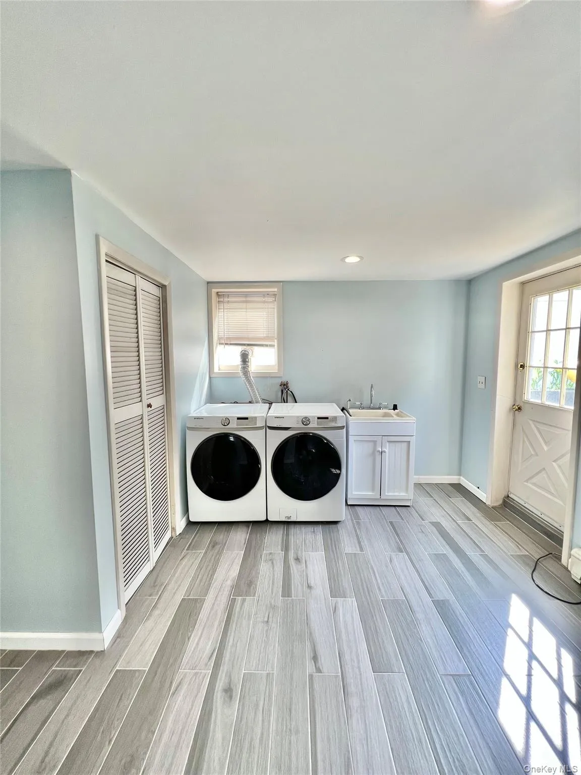 Washroom with light wood-type flooring, cabinet space, a sink, baseboards, and washer and clothes dryer Washroom with light wood-type flooring, cabinet space, a sink, baseboards, and washer and clothes dryer