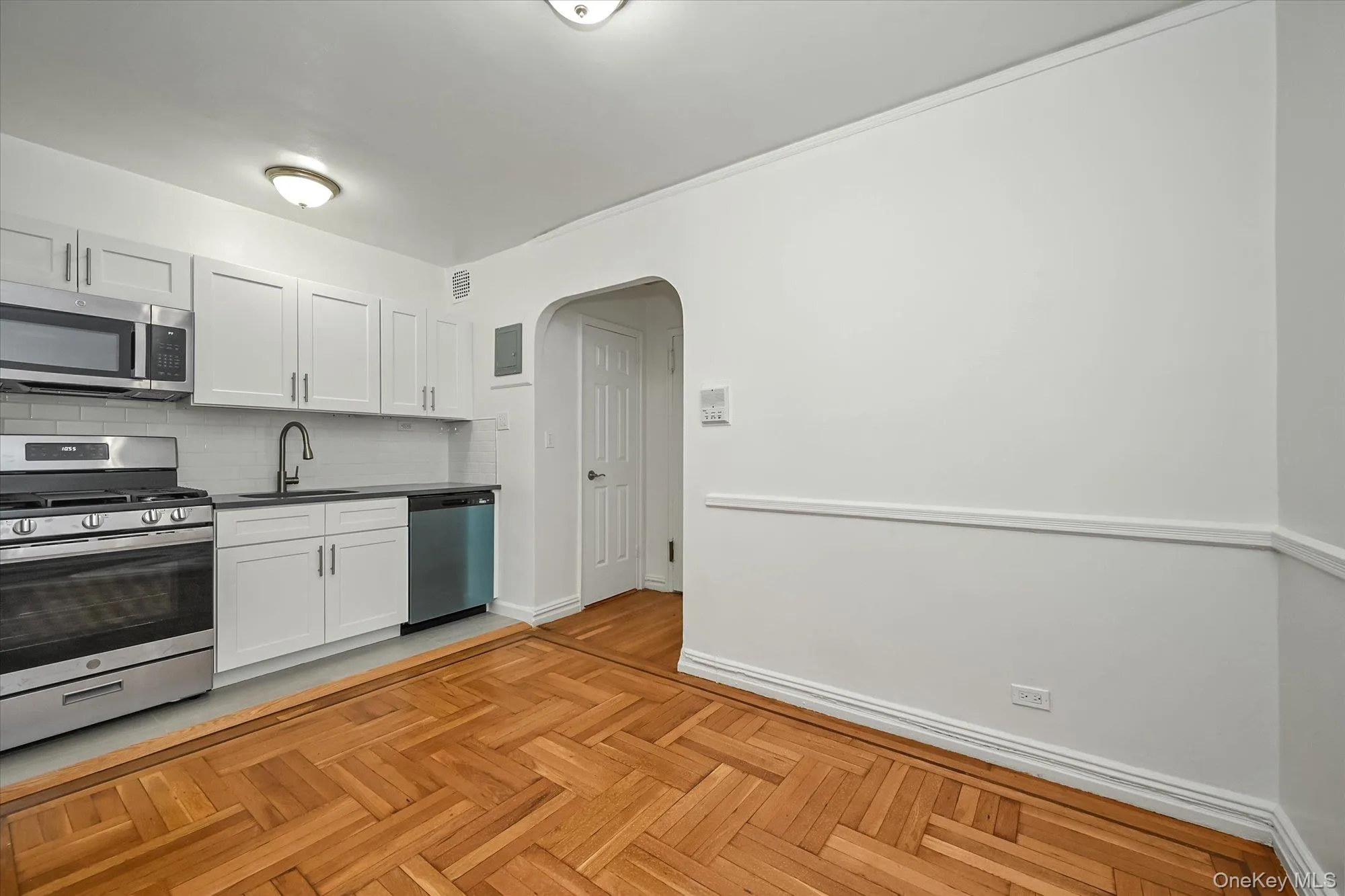 Kitchen featuring arched walkways, stainless steel appliances, quartz countertops, white cabinets, and backsplash Kitchen featuring arched walkways, stainless steel appliances, quartz countertops, white cabinets, and backsplash
