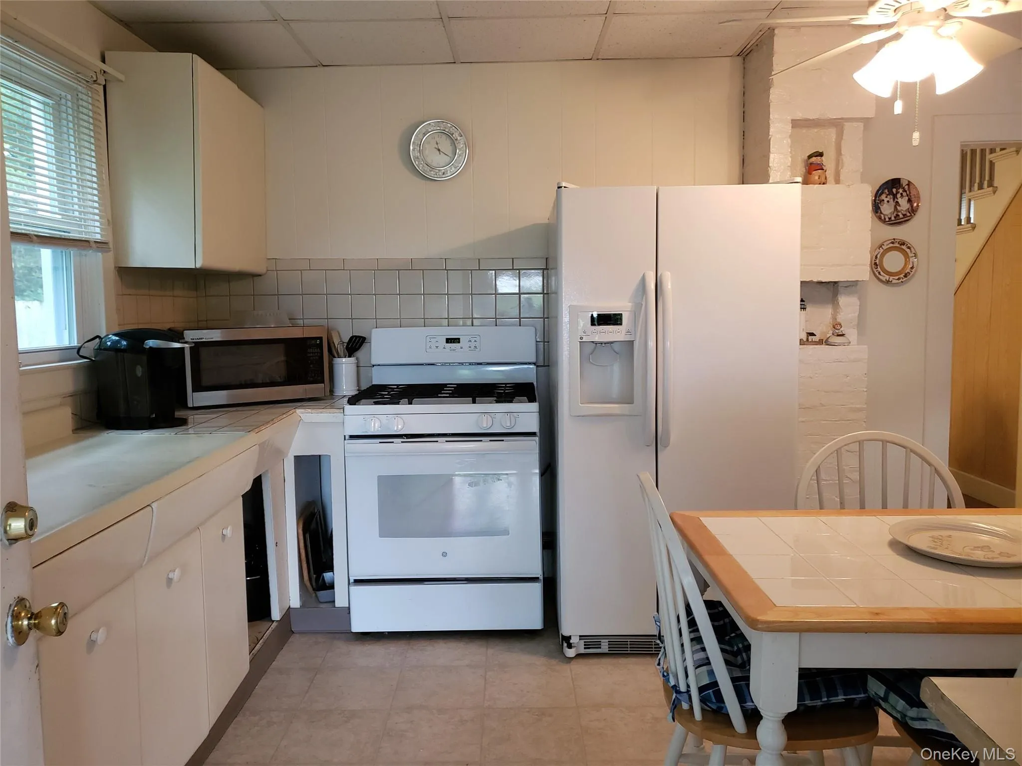 Kitchen with white appliances, a paneled ceiling, a ceiling fan, white cabinetry, and tile counters Kitchen with white appliances, a paneled ceiling, a ceiling fan, white cabinetry, and tile counters