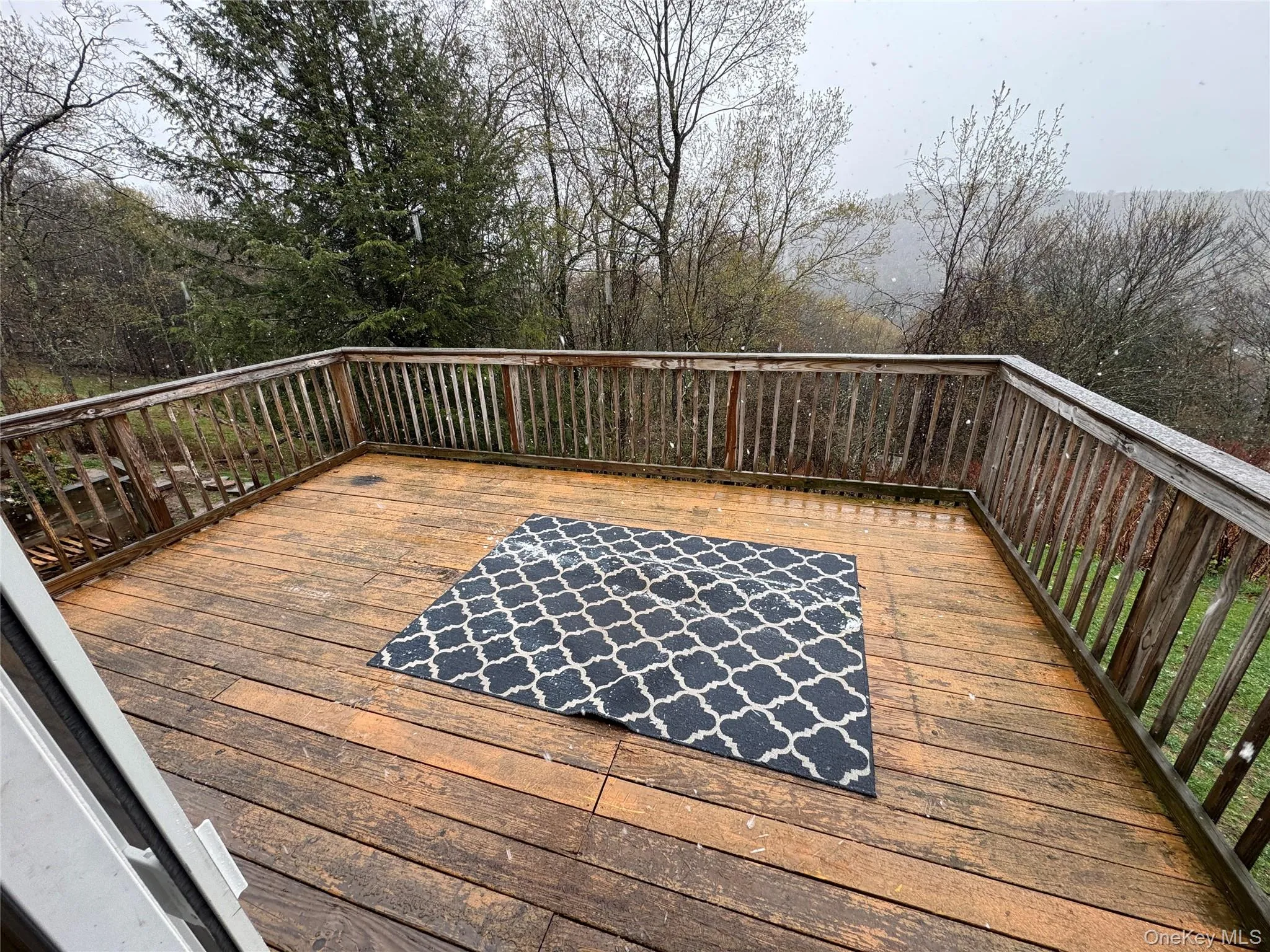 The property features a spacious wooden deck with a railing, offering views of surrounding trees and distant hills The property features a spacious wooden deck with a railing, offering views of surrounding trees and distant hills