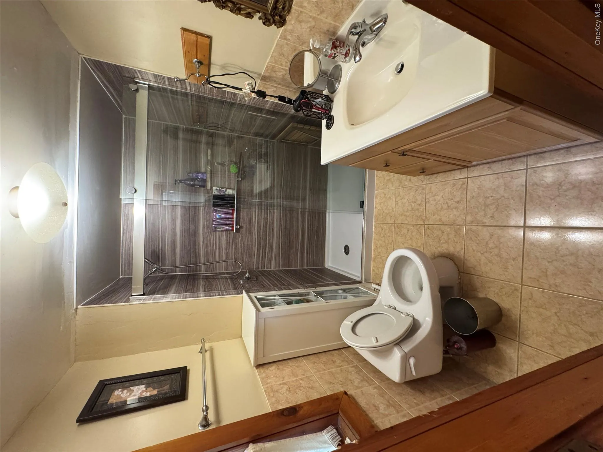 Bathroom featuring a walk in shower with glass enclosure and tiled walls, a vanity with a white sink, and tiled flooring Bathroom featuring a walk in shower with glass enclosure and tiled walls, a vanity with a white sink, and tiled flooring