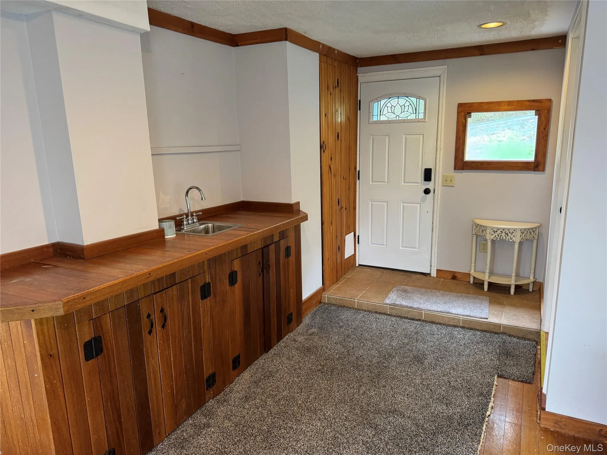 Entry area featuring a wood counter with a wet bar, paneled cabinetry, and a white door with a decorative glass insert Entry area featuring a wood counter with a wet bar, paneled cabinetry, and a white door with a decorative glass insert