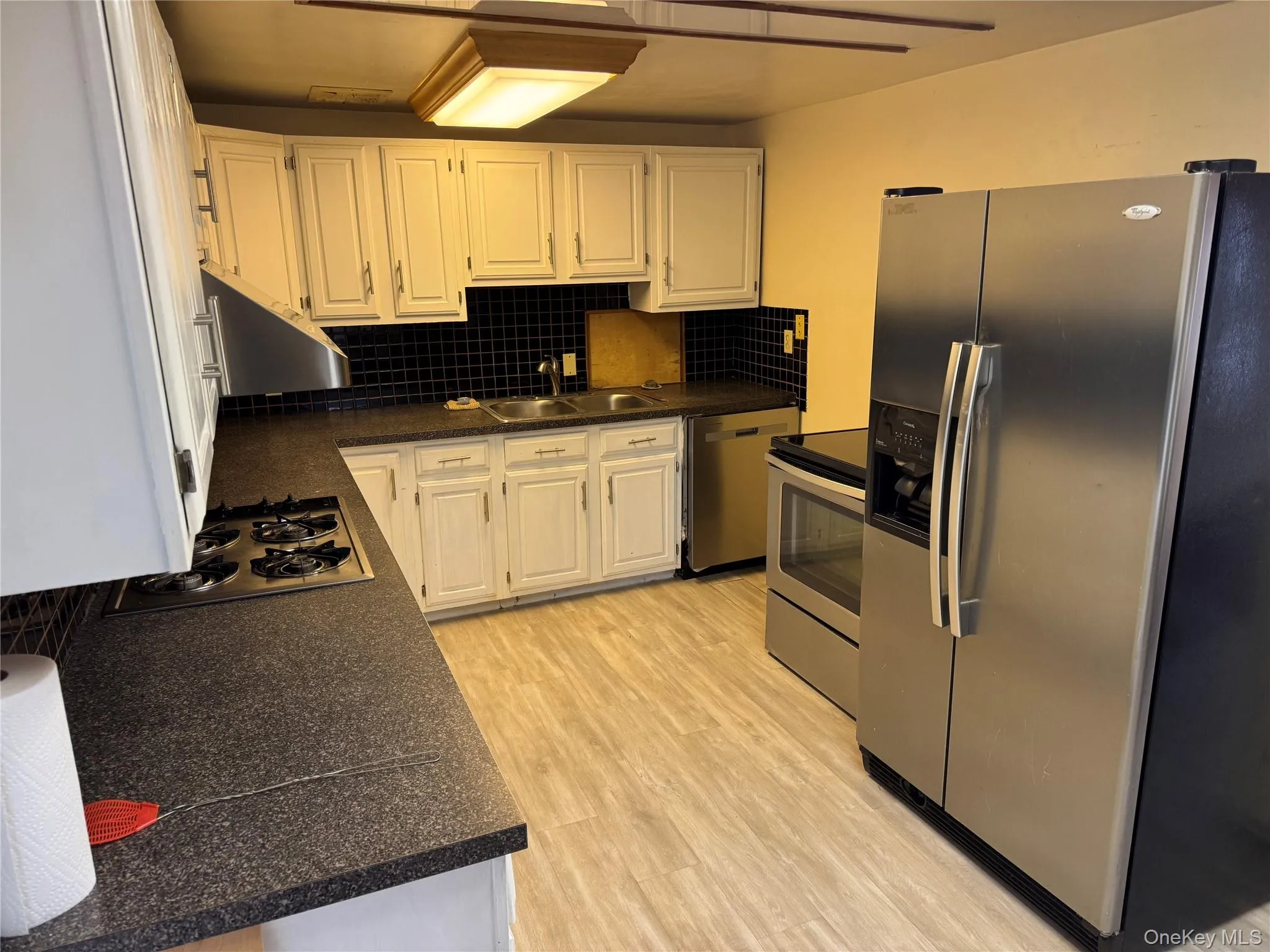 The kitchen features white cabinetry, dark countertops, a black tiled backsplash, and stainless steel appliances The kitchen features white cabinetry, dark countertops, a black tiled backsplash, and stainless steel appliances