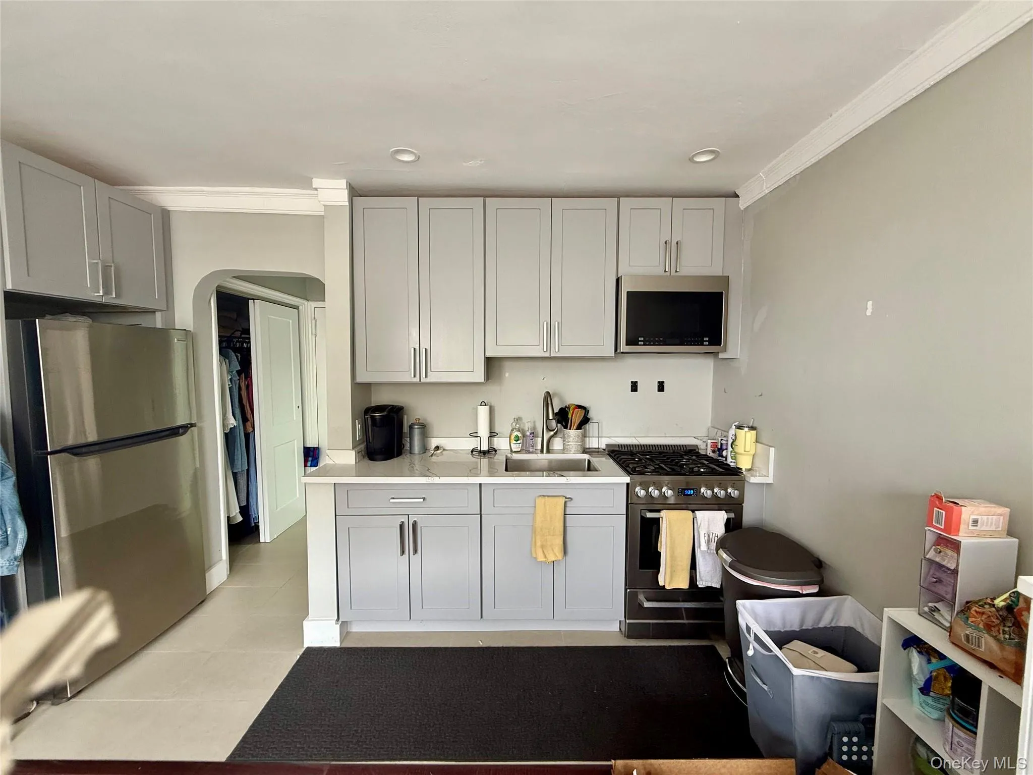 Kitchen featuring stainless steel appliances, a sink, arched walkways, light countertops, and ornamental molding Kitchen featuring stainless steel appliances, a sink, arched walkways, light countertops, and ornamental molding