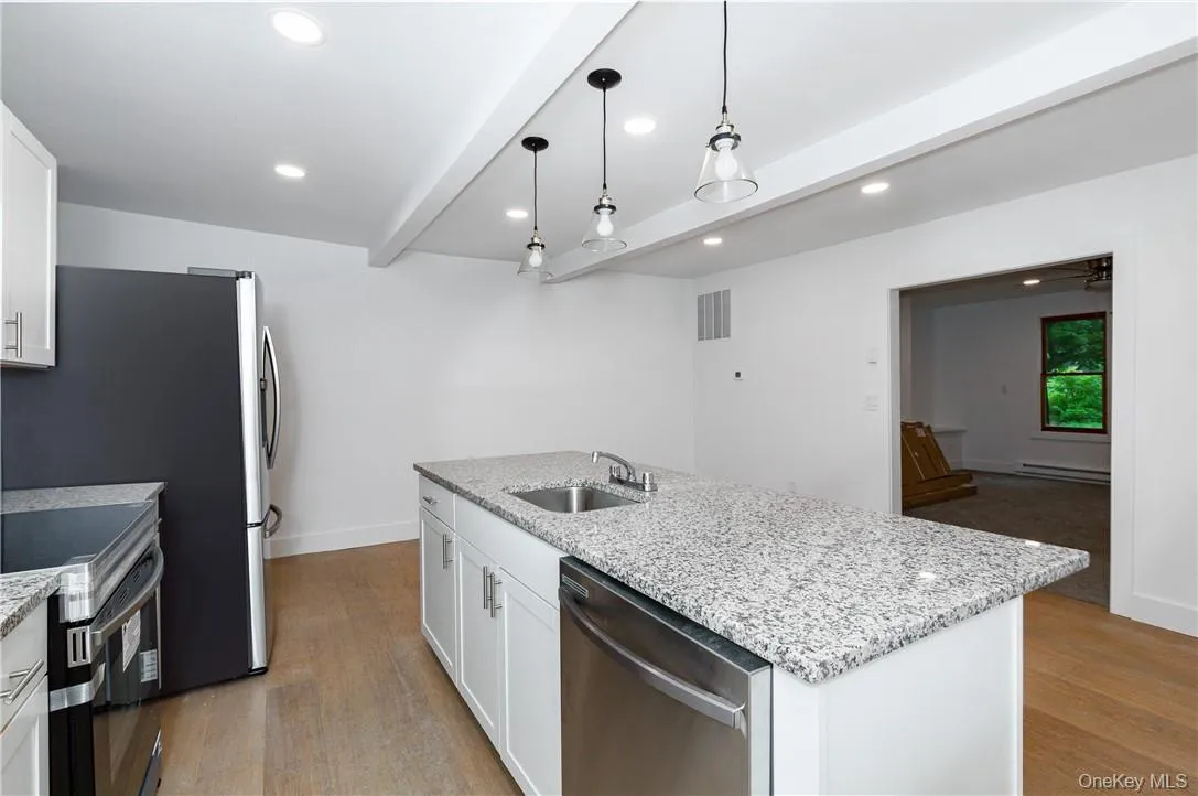 Kitchen featuring stainless steel appliances, sink, white cabinetry, and a kitchen island with sink Kitchen featuring stainless steel appliances, sink, white cabinetry, and a kitchen island with sink