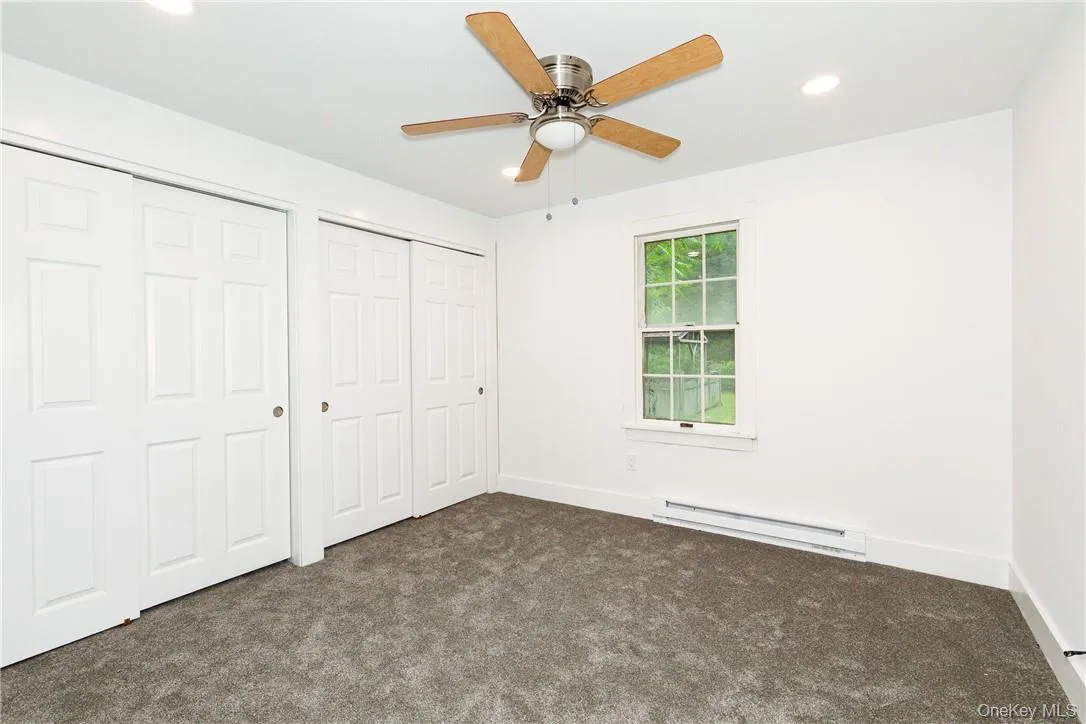 Unfurnished bedroom featuring a baseboard heating unit, two closets, dark colored carpet, and ceiling fan Unfurnished bedroom featuring a baseboard heating unit, two closets, dark colored carpet, and ceiling fan