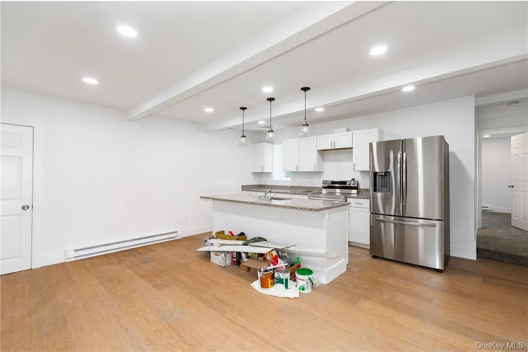 Kitchen with light stone countertops, light hardwood / wood-style flooring, a baseboard heating unit, white cabinets, and appliances with stainless steel finishes Kitchen with light stone countertops, light hardwood / wood-style flooring, a baseboard heating unit, white cabinets, and appliances with stainless steel finishes