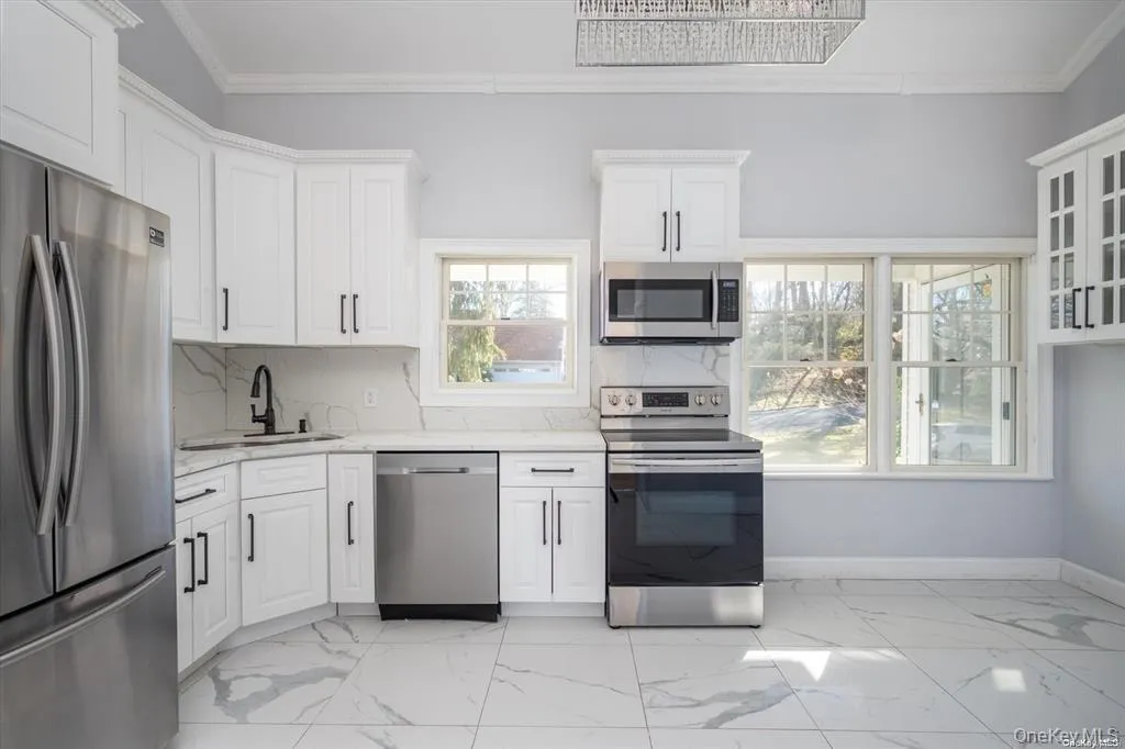 Kitchen featuring stainless steel appliances, crown molding, white cabinetry, light stone countertops, and backsplash Kitchen featuring stainless steel appliances, crown molding, white cabinetry, light stone countertops, and backsplash