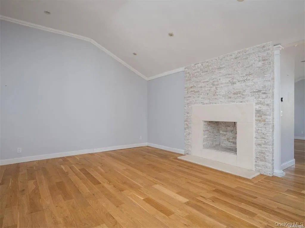 Unfurnished living room featuring crown molding, light wood finished floors, lofted ceiling, and a fireplace Unfurnished living room featuring crown molding, light wood finished floors, lofted ceiling, and a fireplace