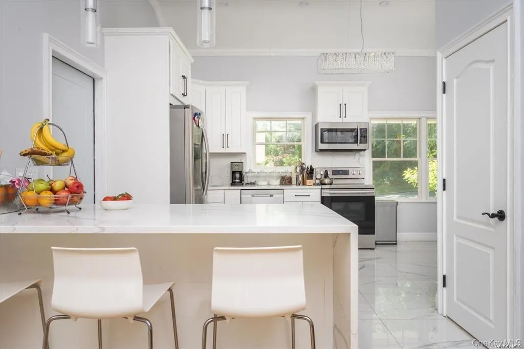 Kitchen featuring stainless steel appliances, a breakfast bar, light stone counters, white cabinetry, and light marble finish flooring Kitchen featuring stainless steel appliances, a breakfast bar, light stone counters, white cabinetry, and light marble finish flooring