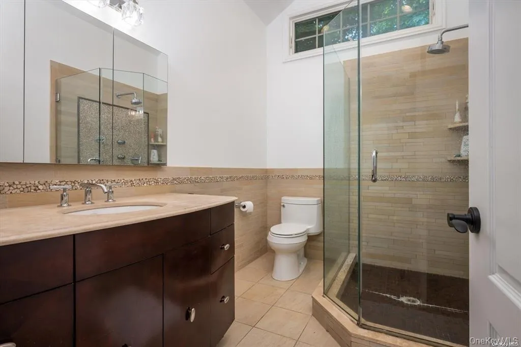 Bathroom with a shower stall, vanity, light tile patterned floors, tile walls, and a wainscoted wall Bathroom with a shower stall, vanity, light tile patterned floors, tile walls, and a wainscoted wall