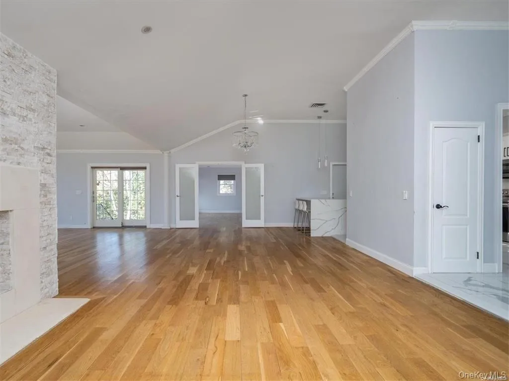 Unfurnished living room with ornamental molding, a stone fireplace, vaulted ceiling, light wood-type flooring, and suspended lighting Unfurnished living room with ornamental molding, a stone fireplace, vaulted ceiling, light wood-type flooring, and suspended lighting
