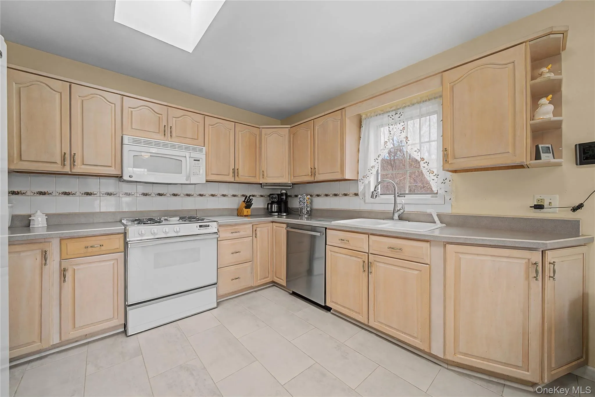 Kitchen with light wood finish cabinetry, white appliances, light countertops, and a skylight Kitchen with light wood finish cabinetry, white appliances, light countertops, and a skylight