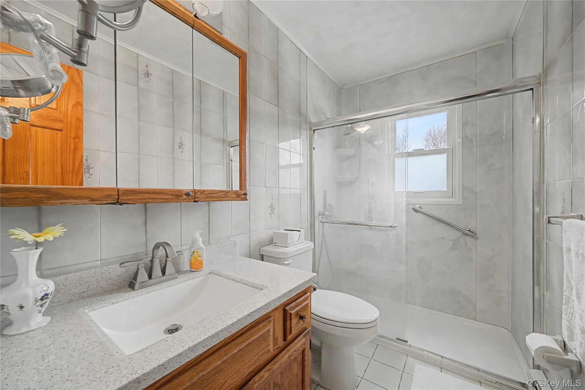 Bathroom with vanity, tile walls, a marble finish shower, and light tile patterned floors Bathroom with vanity, tile walls, a marble finish shower, and light tile patterned floors