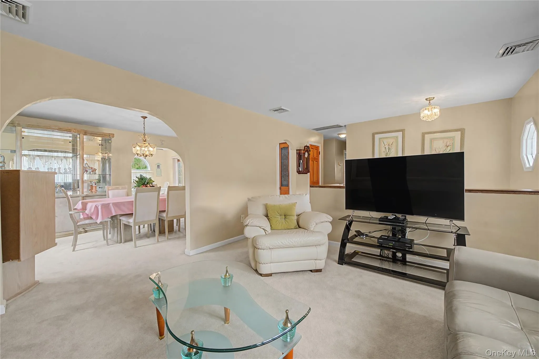 Living room with plenty of natural light, light colored carpet, suspended lighting, and arched walkways Living room with plenty of natural light, light colored carpet, suspended lighting, and arched walkways