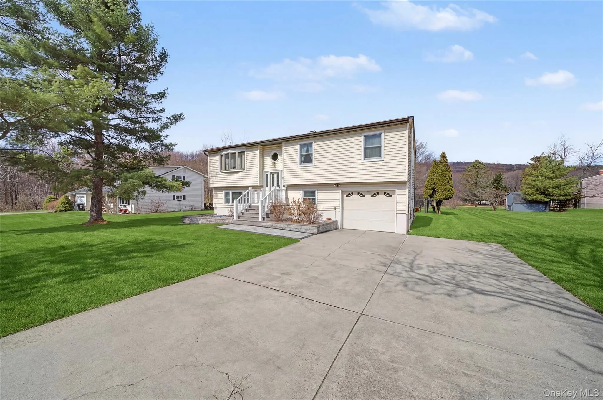 Bi-level home featuring a front lawn, a garage, and concrete driveway Bi-level home featuring a front lawn, a garage, and concrete driveway